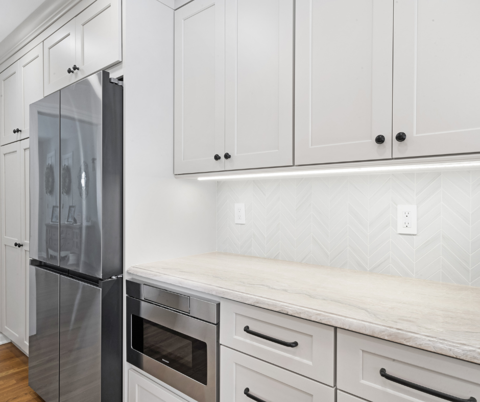 Kitchen with under cabinet lighting, white shaker cabinets, stainless steel appliances and black hardware.